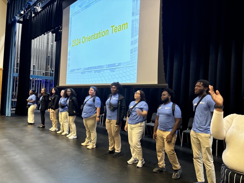 Orientation leaders standing on stage in front of a sign that says 2024 orientation team.