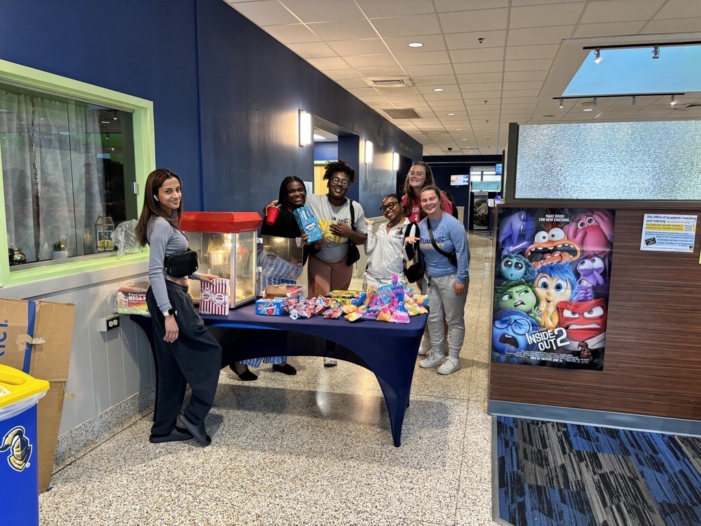 Students standing in front of a popcorn machine next to an Inside Out 2 poster during a Welcome Program event.